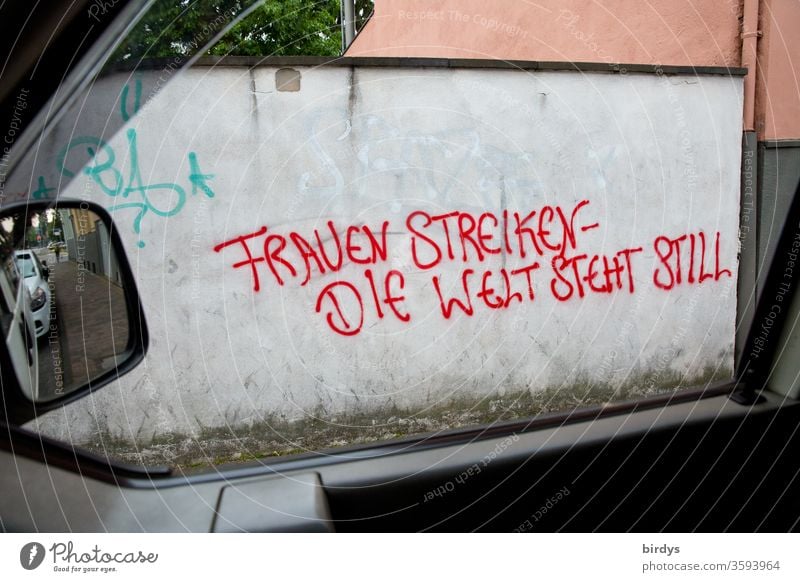 Grafitti mit Text auf einer Mauer durch ein Seitenfenster eines Autos fotografiert." Frauen streiken- die Welt steht still." Gleichberechtigung, Hinweis auf die wichtige Rolle der Frau in der Welt und der Ruf nach Gleichstellung.