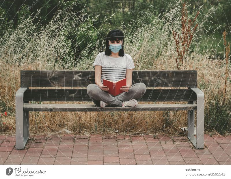 Frau mit medizinischer Maske, die auf einer Bank sitzend ein Buch liest Coronavirus Junge Frau Covid-19-Virus lesen träumen sich[Akk] entspannen