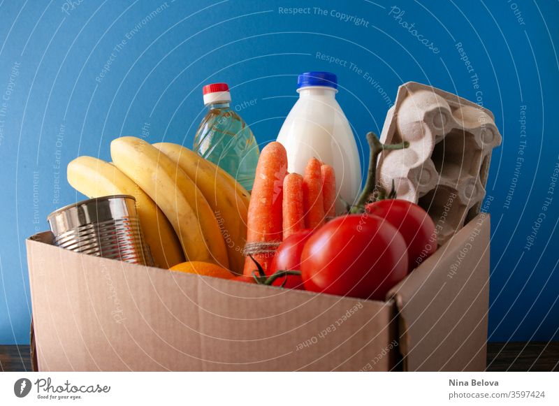 Lebensmittellieferung.box mit Lebensmittelgeschäft. Auf blauem Hintergrund. Tomaten,Bananen,Milch,Eier,Konserven,Öl. Spende. schenken Kasten Dienst Geben