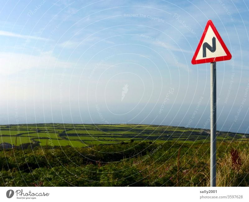 kurvig gehts runter zum Meer... Verkehrschild Kurve Straßenschild Hinweis Hinweisschild Mast Landschaft England Cornwall Hügel Feld Hecke schönes Wetter Natur