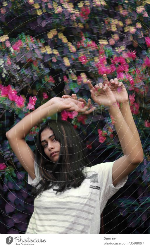 Junge Frau von mittlerer Länge winkt mit erhobenen Händen vor einem bunten Blumenbusch. Glitch-Effekt. Jugendliche Jugendkultur Porträt Porträtmalerei Störung