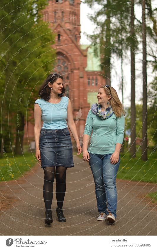 lebensnotwendig | Freundschaft – zwei junge Frauen gehen spazieren und unterhalten sich, im Hintergrund eine Kirche Freundinnen Spaziergang miteinander zusammen