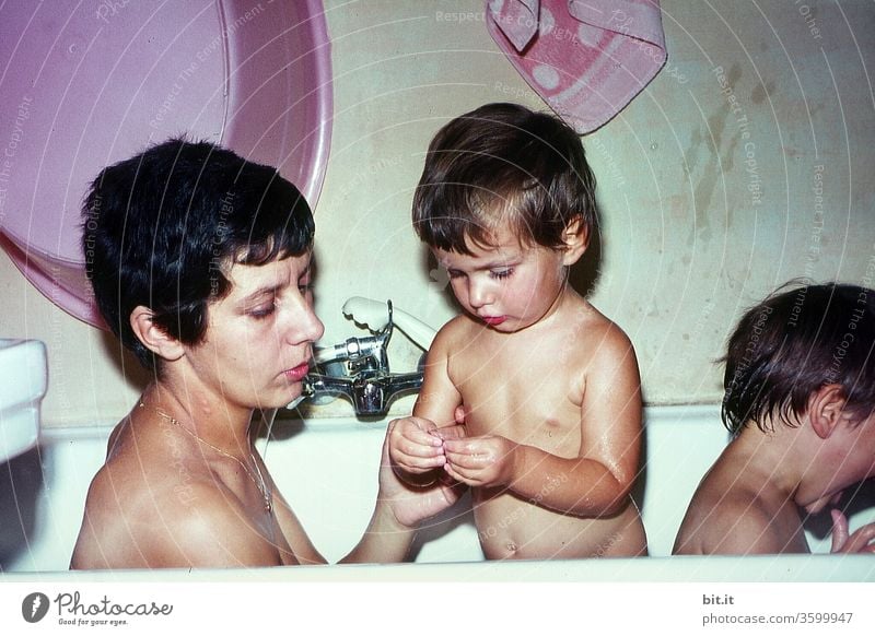 alt l Junge, hübsche, attraktive Mutter mit kurzen, schwarzen Haaren, badet zusammen mit ihren zwei Kindern in der Badewanne der 60er Jahre. Fürsorgliche, aufmerksame Mama, kümmert sich liebevoll, interessiert, zugewandt um Frage vom neugieriegen Kind.