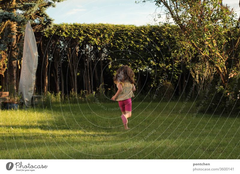 Ein Kind im Vorschulalter läuft glücklich durch den Garten. Rückansicht. Sommer. Kindheit laufen garten kindheit wiese vergnügen freude Spielen Fröhlichkeit