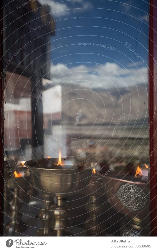 Antike tibetische Öllampen hinter einer Fensterscheibe, in der sich ein Gebirgszug des Himalayas spiegelt. Felsen Natur Gebirge Berge Tal hoch Farbfoto Himmel