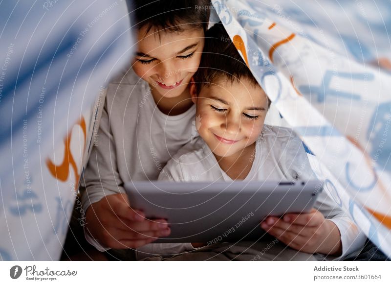 Glückliche Brüder sehen sich gemeinsam ein Video auf einem Tablet an zuschauen Karikatur Zusammensein Tablette Bruder Geschwisterkind Pyjama Decke benutzend