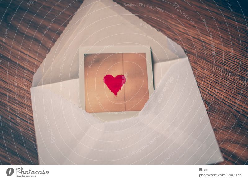 Foto mit rotem Herz wird in einem Briefumschlag versendet Post verschicken Liebesbrief Liebesgrüße verliebt Kommunikation schreiben Polaroid weiß Holz