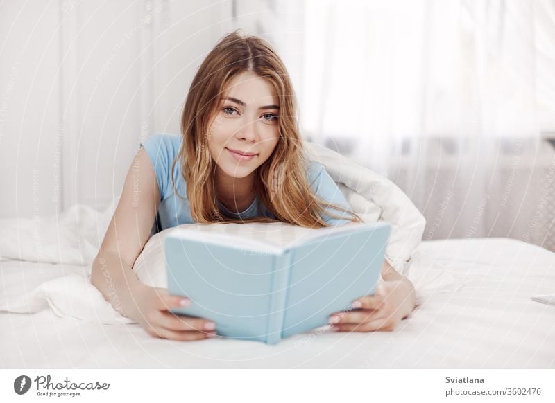 Hübsches Mädchen im blauen Pyjama, ein Buch lesend, auf dem Bett im Schlafzimmer liegend. Ausbildung, Erziehung, Hobbys. Raum lautet Lügen heimwärts Freizeit