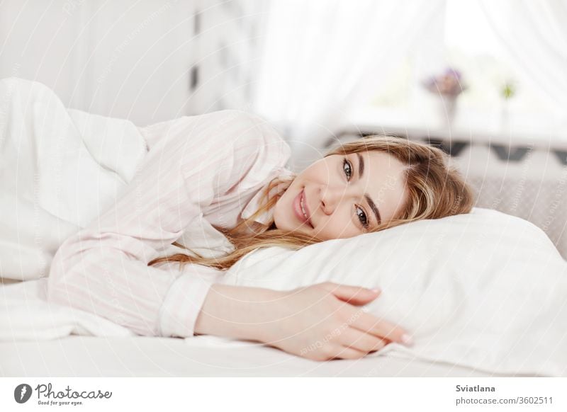 Ein junges attraktives Mädchen in gestreiften Pyjamas liegt morgens in ihrem Schlafzimmer im Bett. Seitenansicht Morgen Frau schön heimwärts schlafen Kopfkissen