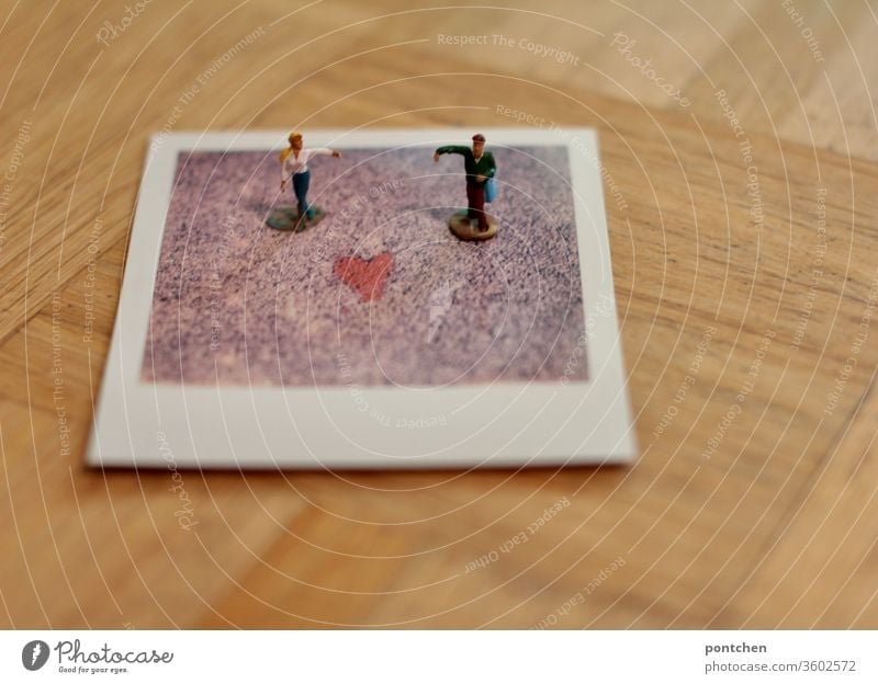 Zwei Figuren Mann und Frau stehen mit ausgebreitetem Arm auf einem Polaroid mit einem Herz. Liebe, symbolik. PoC. geschlechterrollen emanzipation einhaken tanz
