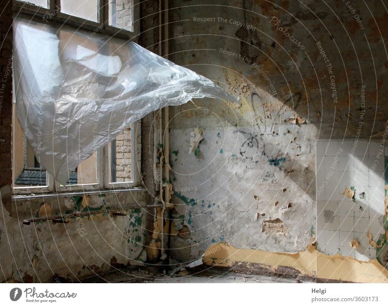 Durchzug - in einem alten maroden Gebäude mit zerstörtem Fenster weht ein Plastikvorhang vom Wind in die Höhe und lässt das Sonnenlicht herein Haus Wand Mauer