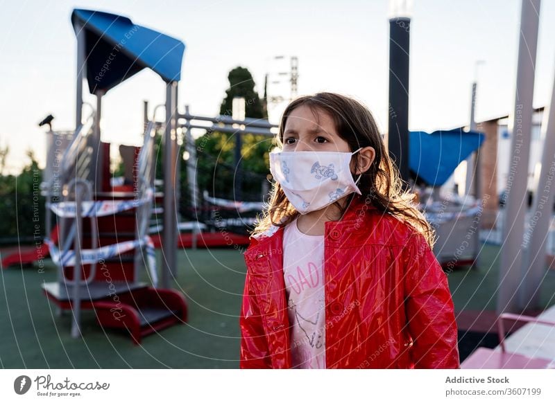 Stirnrunzelndes Mädchen mit medizinischer Maske auf dem Spielplatz Kind Mundschutz beunruhigt Ausbruch Coronavirus Großstadt ethnisch Kindheit modern urban