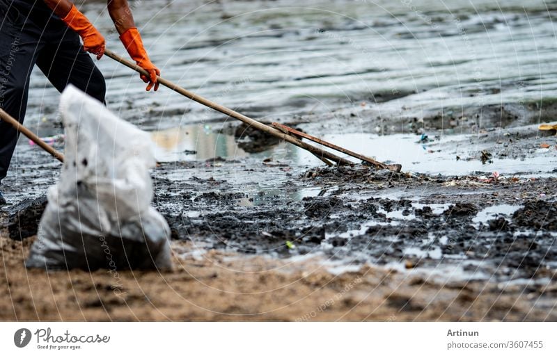 Freiwillige Helfer benutzen den Rechen, um den Müll aus dem Meer zu fegen. ฺBeach Reiniger, der den Müll am Meeresstrand in einer durchsichtigen Plastiktüte sammelt. Freiwillige, die den Strand säubern. Aufräumen von Müll am Strand.