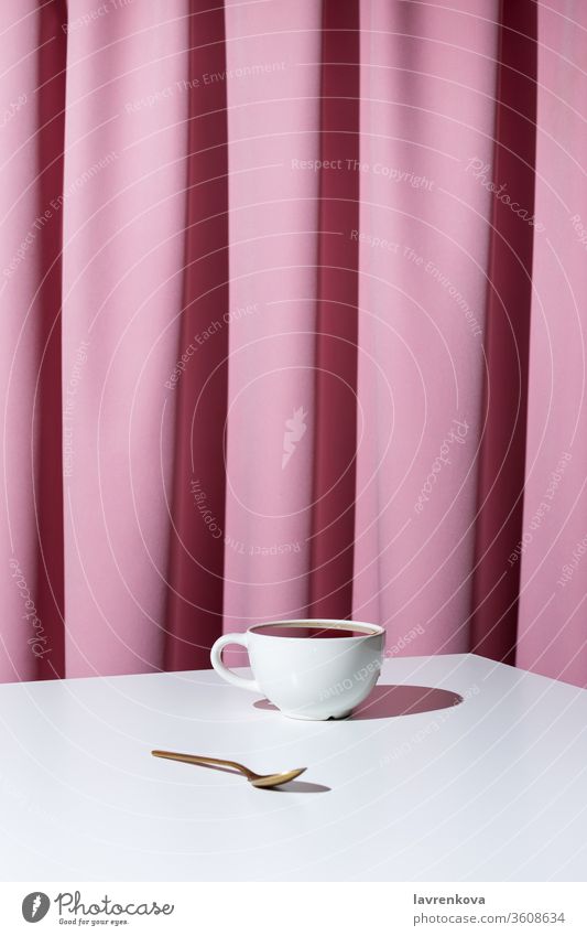 Tasse Tee oder Kaffee auf weißem Tisch vor rosa Draperie, selektiver Fokus Aroma Getränk schwarz Koffein Gardine Vorhang trinken Espresso heiß im Innenbereich
