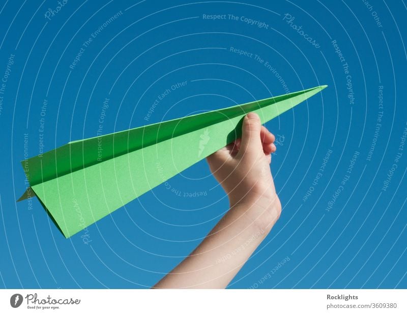 Grünes Reisekonzept mit einem grünen Papierflugzeug gegen blauen Himmel Flugzeug Aspirationen Jungen Kind fliegen Inspiration Freiheit menschlich Hand Ideen