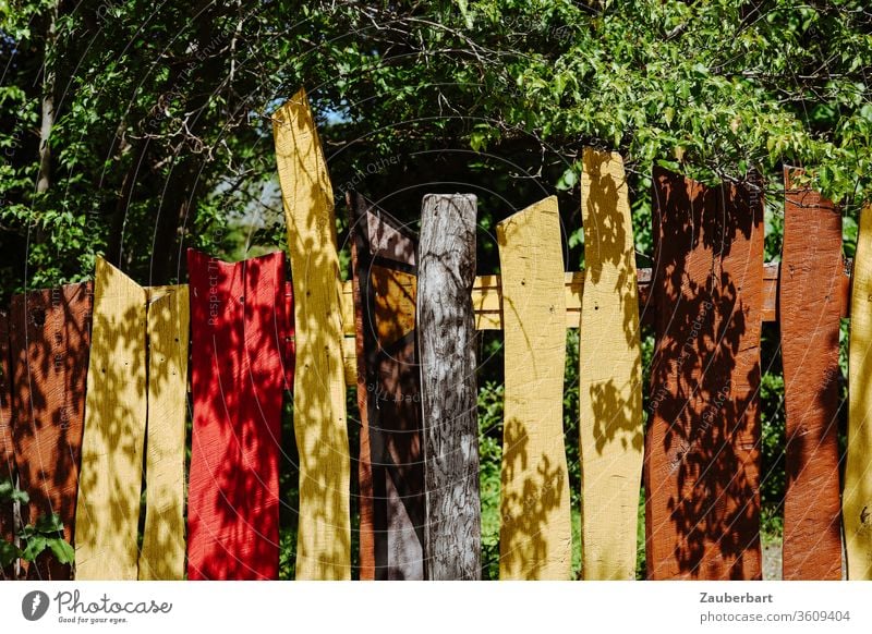 Bunter Holzzaun mit gelben, brauen und roten Latten, Blätter und Schattenwurf Zaun bunt braun Holzlatten Baum Kontrast krumm Grenze Grundstück Garten Nachbar