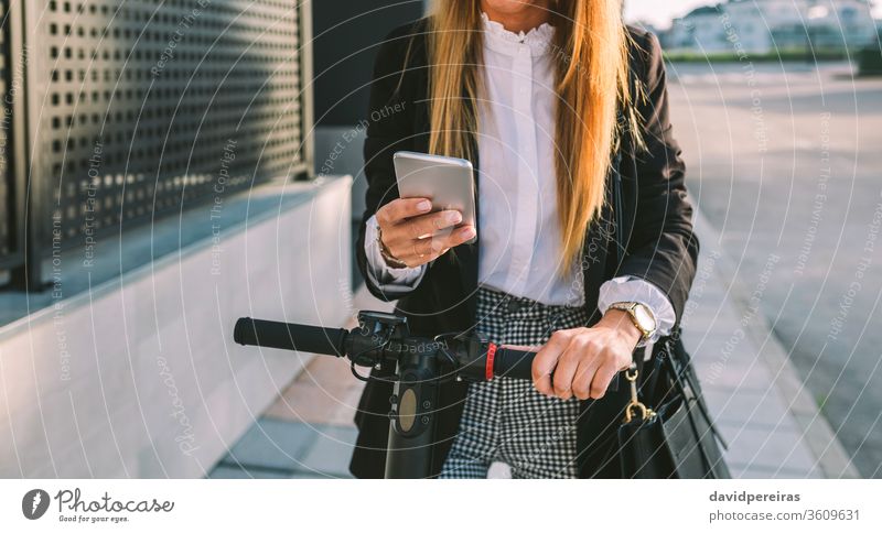 Nicht erkennbare Geschäftsfrau mit E-Scooter beim Blick auf das Handy Tretroller unkenntlich Frau Großstadt Straße Mode Mobile Arbeiter stylisch Menschen