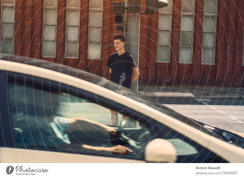 Porträt eines einsamen jungen Mannes, bei dem ein Auto durch das Bild fährt Jugendlicher schön Junge Gebäude PKW lässig Kaukasier selbstbewusst Kultur Laufwerk