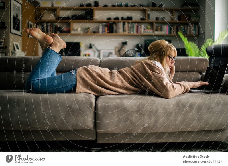 Nachdenkliche Frau arbeitet zu Hause am Laptop Browsen freiberuflich Projekt benutzend Telearbeit Lügen Sofa Arbeit abgelegen ernst Brille Apparatur Internet