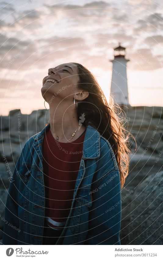 Glückliche Frau gegen Sonnenuntergangshimmel und Leuchtturm reisen Lachen Himmel wolkig Peggys-Bucht Kanada jung Abend Abenddämmerung Dämmerung Lächeln lässig