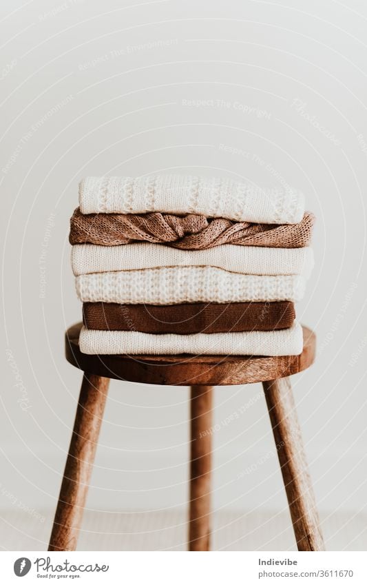 Zusammensetzung der Damenmode. Warme weibliche Strickpullover aus Wolle für den Winter, Pullover stapeln sich auf einem Holzhocker auf weißem Hintergrund. Modernes Kleidungskonzept für Zeitschrift, Blog, soziale Medien.
