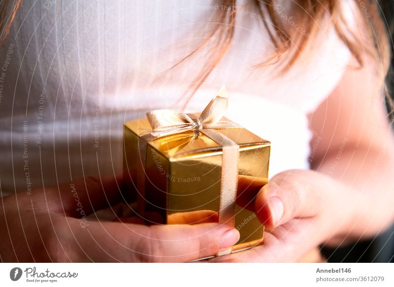 Frauenhände halten goldene Geschenkbox, Feiertagsgeschenk, Geburtstag, Weihnachten, Vater oder Mutter, Valentinstag Nahaufnahme Hintergrund Familie Business