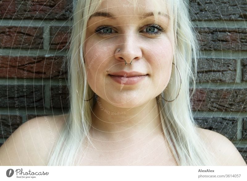 Portrait einer jungen blonden Frau vor einer Backsteinwand Mädchen junge Frau schön lächeln lange Haare Ohrringe blaue Augen Haut 19 18-20 Jahre 15-20 Jahre alt