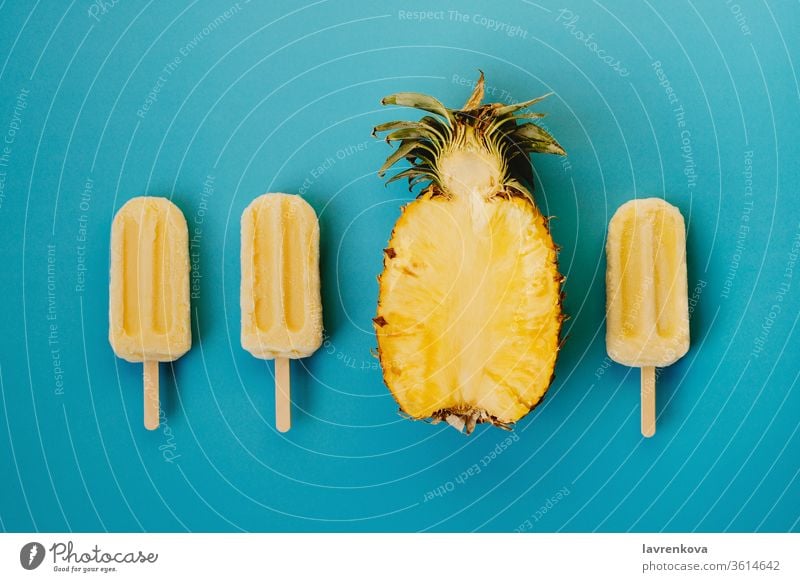 Tropischer Flachschlag aus drei veganen Eis am Stiel und der Hälfte einer reifen Ananas auf cyanfarbenem Hintergrund saisonbedingt Sommer kalt Dessert
