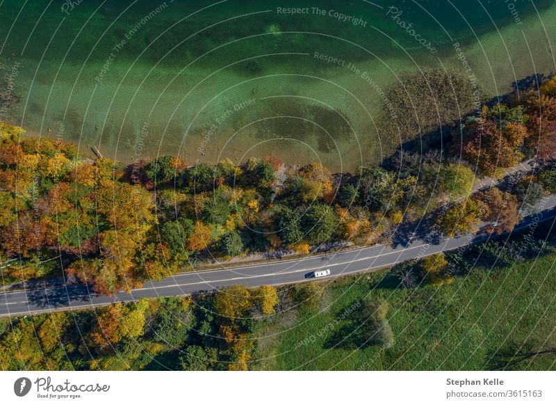 Luftaufnahme der Straße mit einem Auto im Herbstwald neben einem toukisfarbenen See. PKW Top Landschaft Dröhnen Autobahn reisen schön Transport Antenne Wald