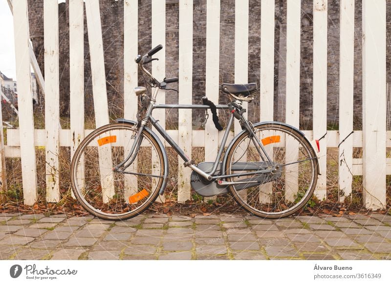 Graues, altes, Vintage- und Retro-Fahrrad, mit Vorhängeschloss an einem weiß gestrichenen Holzzaun in der Stadt Gent, in Belgien, Europa. grau altehrwürdig