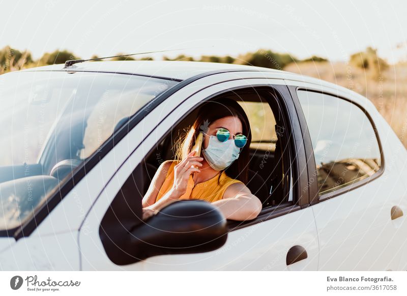junge Frau in einem Auto, die ein Mobiltelefon benutzt und eine Schutzmaske trägt. Sommersaison. Konzept zur Prävention des Coronavirus PKW Handy Virus
