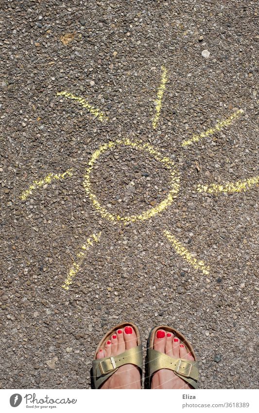 Weibliche Füße in Birkenstocks stehen vor einer gemalten Sonne aus Kreide auf der Straße. Sommer. Sonnenschein somerlich Sandalen weiblich Frau