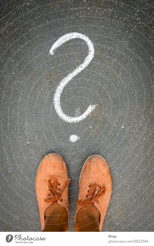 Füße stehen vor einem Fragezeichen, das mit Kreide auf den Boden gemalt ist. Frage, Ratlosigkeit, Unentschlossenheit. Entscheidung ratlos Verwirrung