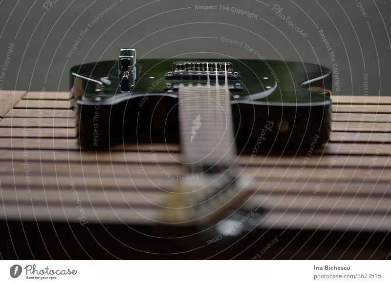 Eine schwarze E-Gitarre auf einem Holzbrett-Tisch fotografiert aus der Gitarren Kopf Perspektive. Der Fokus liegt am Seitenhalter und Knopf. Egitarre