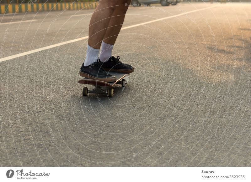 Nahaufnahme der Füße eines jungen Teenagers mit zerrissenen schwarzen Turnschuhen auf seinem Skateboard, der auf einer leeren Straße fährt, während die weiße Linie auf der Straße seine weißen Socken ergänzt und auch als Führungslinie in der Richtung dient, in die er sich bewegt.