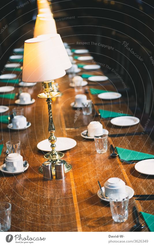 ein gedeckter Tisch / Tafel mit leeren Plätzen corona abstand aufgedeckt Geschirr Lampenlicht Einladung Treffen Business meeting Leere verlassen Pandemie