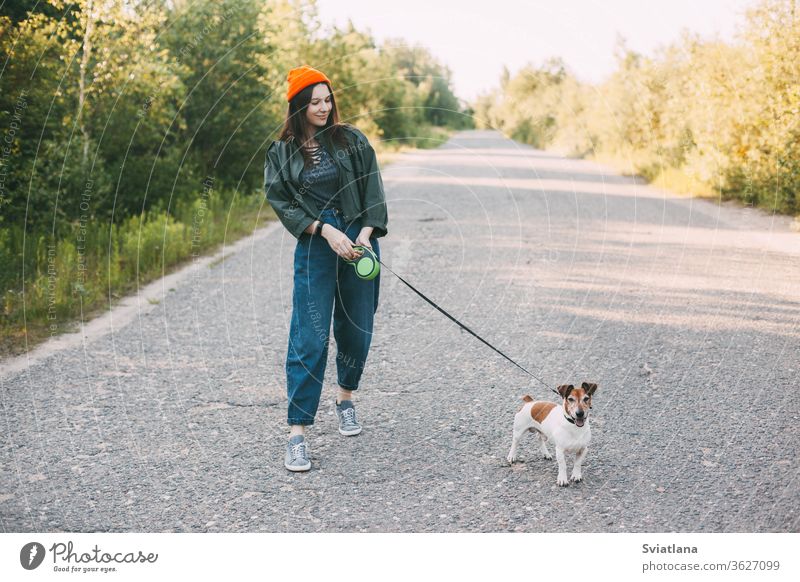 Süßes modernes Teenager-Mädchen in grüner Jacke und orangem Hut geht mit ihrem Hund in der Natur spazieren. Haustier, Pflege, Freundschaft. Park jung laufen