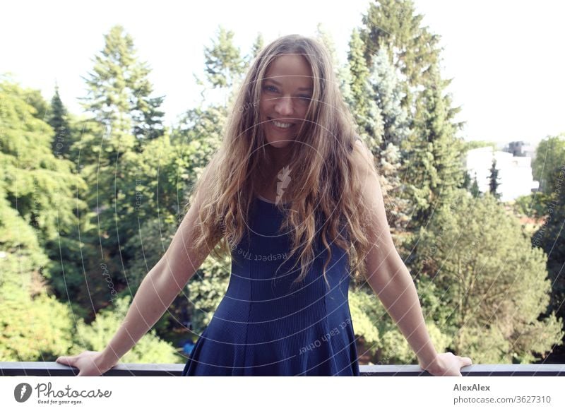 Portrait einer lachenden jungen Frau auf dem Balkon vor Bäumen Blauer Himmel intensiv Mädchen Erwachsene Porträt Tag Haut Sonnenlicht selbstbewußt