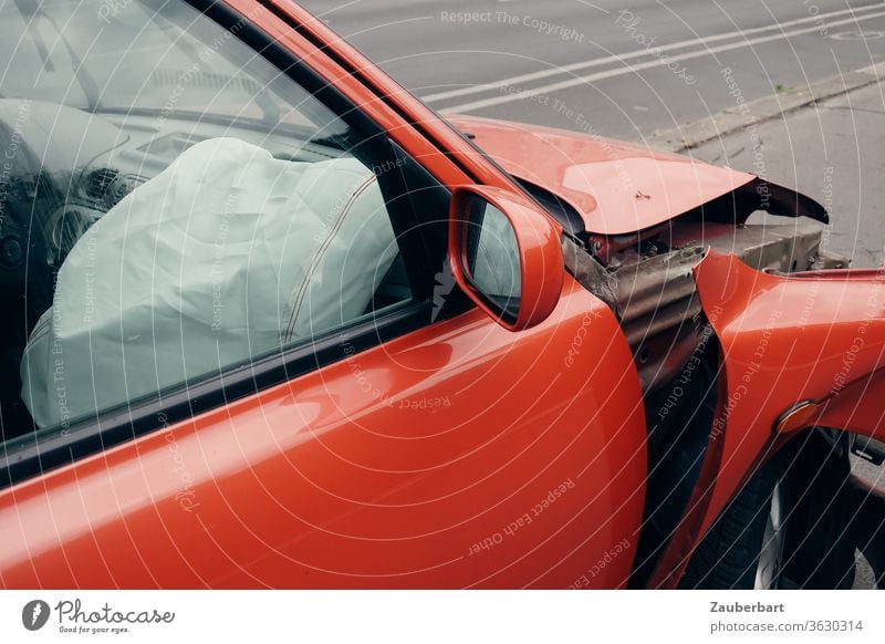 Airbag auf der Beifahrerseite eines roten Autos mit verbeultem Kotflügel Unfall Beule Totalschaden Straße Straßenverkehr Rückspiegel Blech Schaden Versicherung