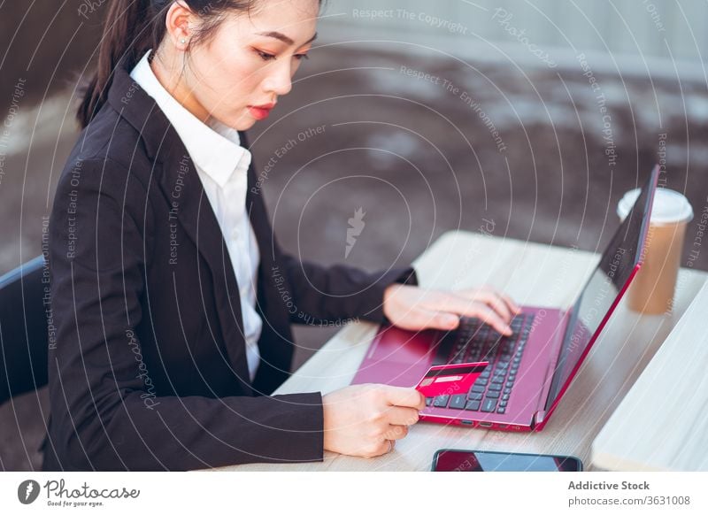 Junge Geschäftsfrau, die mit Kreditkarte und Laptop bezahlt Frau benutzend beschäftigt Smartphone bezahlen online formal jung asiatisch ethnisch ernst Apparatur
