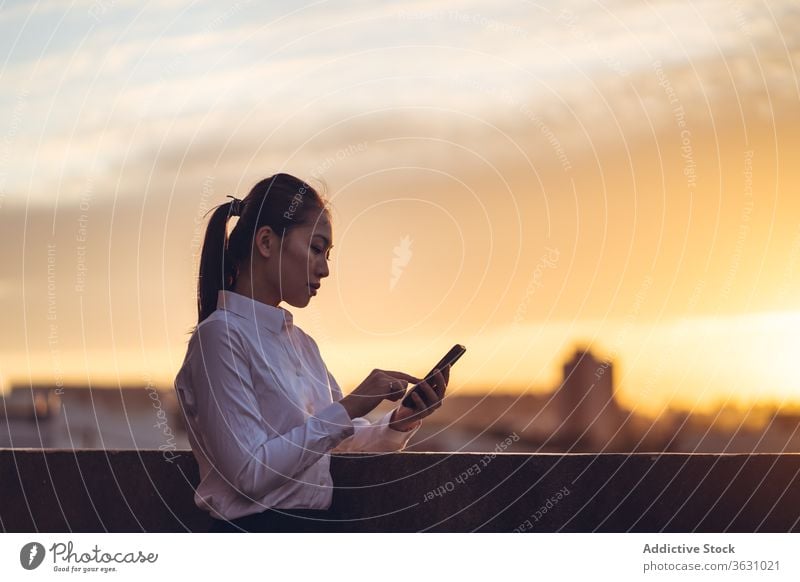 Junge beschäftigte Frau benutzt Smartphone auf dem Dach Geschäftsfrau benutzend ernst Fokus Nachricht Browsen jung asiatisch ethnisch formal Dachterrasse Gerät