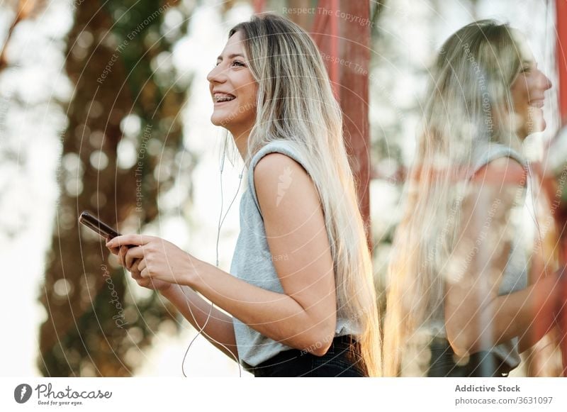 Fröhliche Frau mit Kopfhörern mit Smartphone auf der Straße Glück heiter zuhören benutzend Browsen jung Musik genießen Gerät Apparatur Lifestyle Lächeln online