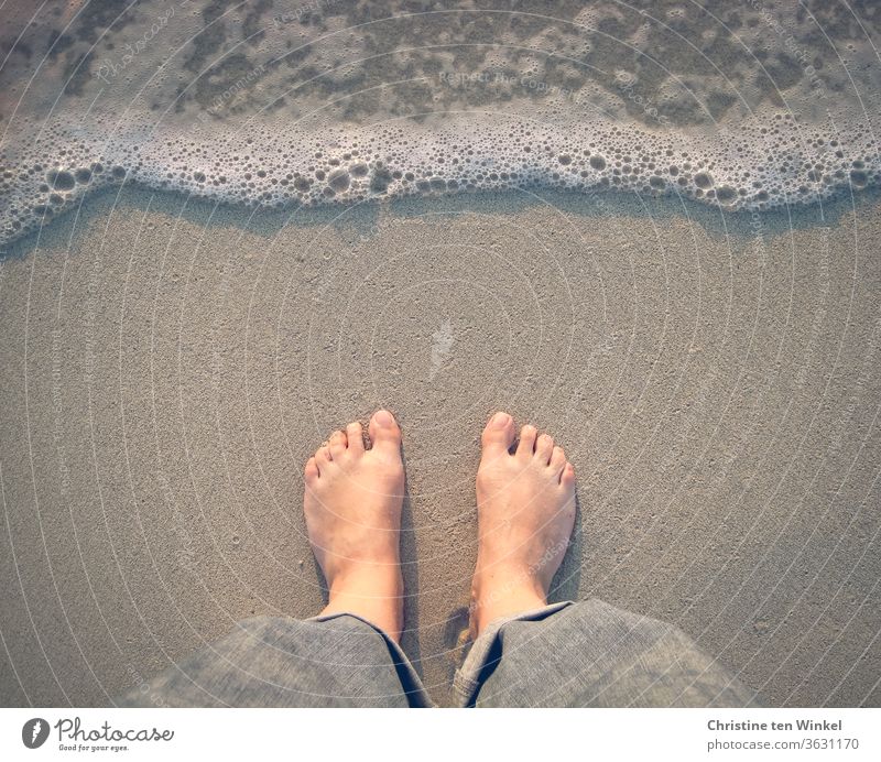 symmetrie | Am Nordseestrand stehen und warten und zuschauen, bis das auflaufende schaumige Wasser die eigenen Füße berührt. Watt Sandstrand nass