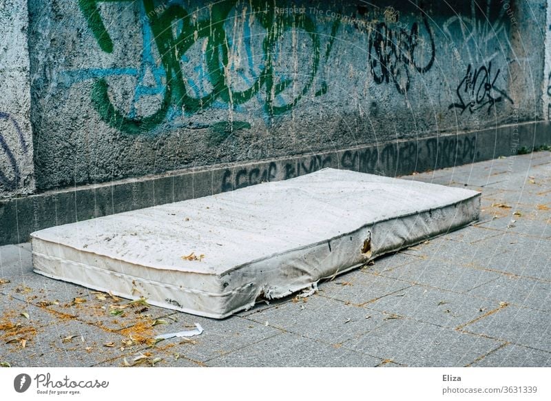 Eine alte Matratze auf der Straße vor Graffiti. Konzept Wohnungsnot und Obdachlosigkeit. Wohnungssuche draußen schlafen Verzweiflung Armut Schlafplatz obdachlos