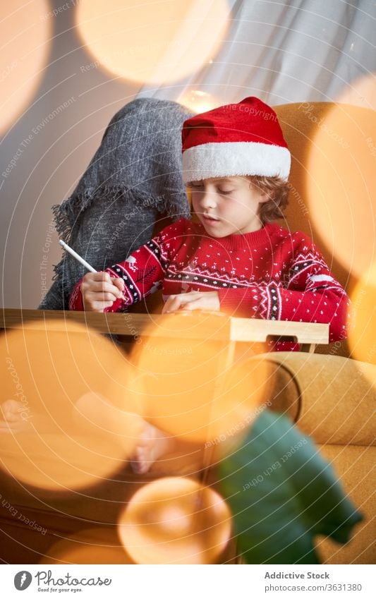 Junge in Weihnachtskleidung im gemütlichen Sessel sitzend Weihnachtsmütze Weihnachten Feiertag Bleistift Armsessel Glück Komfort heimisch Pullover froh heiter