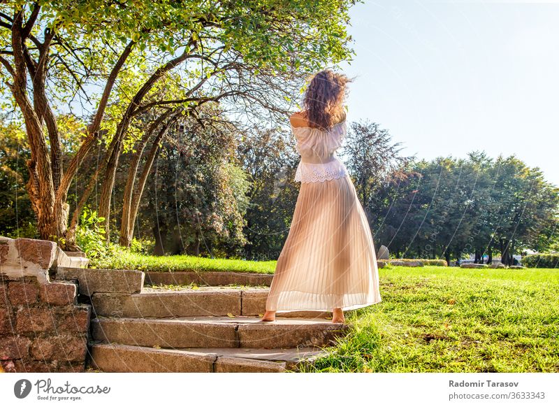 junges Mädchen in leichtem Kleid, das an einem sonnigen Sommertag mit dem Rücken im Park steht Licht Frau Schönheit Natur Lifestyle im Freien schön Person