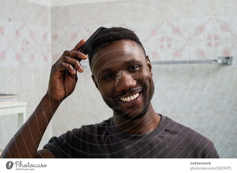 Gutaussehender schwarzer Mann lächelt und kämmt Haare im Badezimmer Kamm Kämmen Behaarung Gesicht Frisur 1 Mensch afrikanische ethnische Zugehörigkeit Lächeln