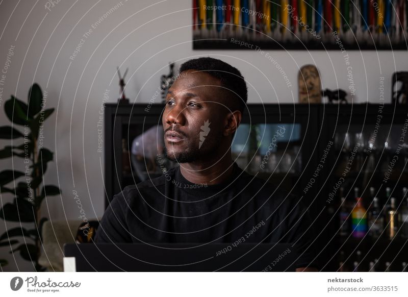Porträt eines gut aussehenden schwarzen Mannes, der im Wohnzimmer sitzt und wegschaut 1 Mensch afrikanische ethnische Zugehörigkeit Lifestyle 20-30 Jahre alt