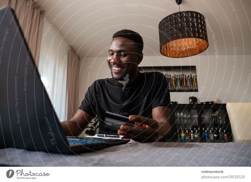 Junger schwarzer Mann lächelt beim Online-Einkauf vom Wohnzimmer aus online Kreditkarte Online-Shopping Bankkarte Lächeln Fröhlichkeit positive Emotion Kauf