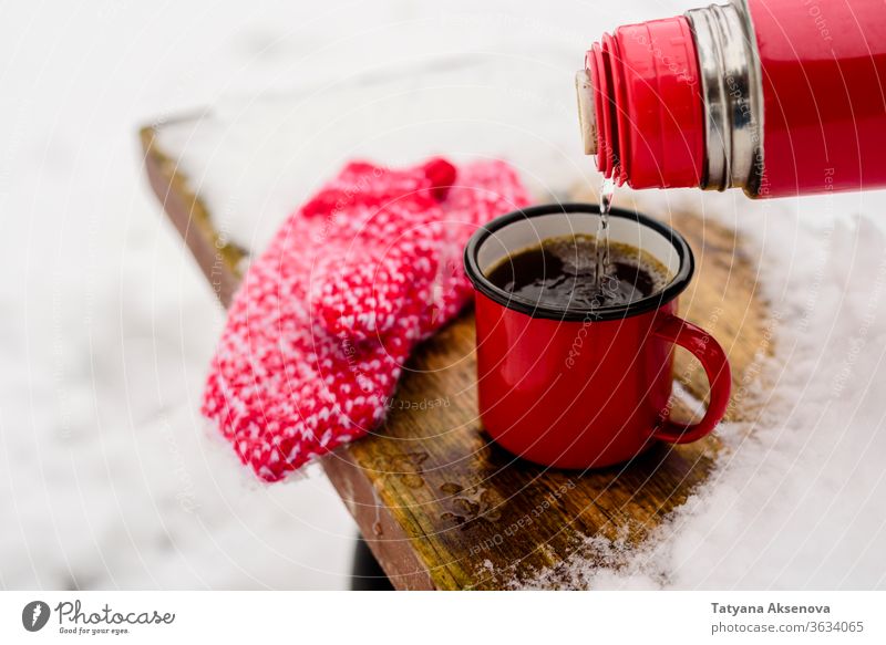 Rote Tasse mit heissem Kaffee oder Tee trinken auf Schnee im Winter heiß Becher kalt Fäustlinge rot warm Weihnachten Feiertag weiß Getränk Saison im Freien